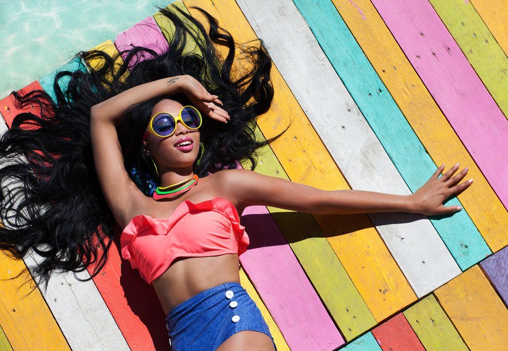 A woman in a bikini and sunglasses is laying on a colorful wooden deck.