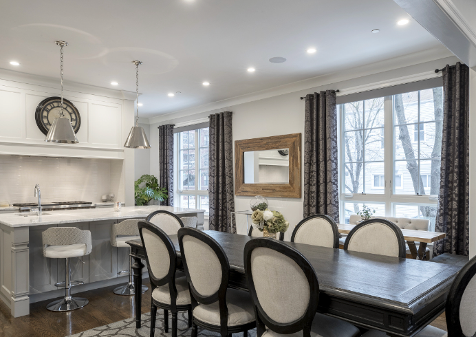 A dining room with a table and chairs and a kitchen in the background.