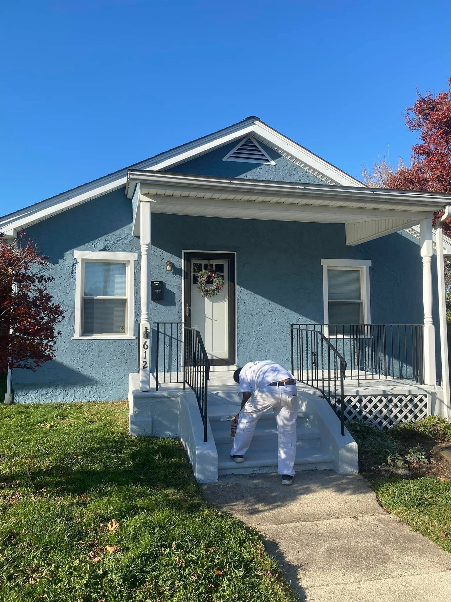 A man is painting the front of a blue house.