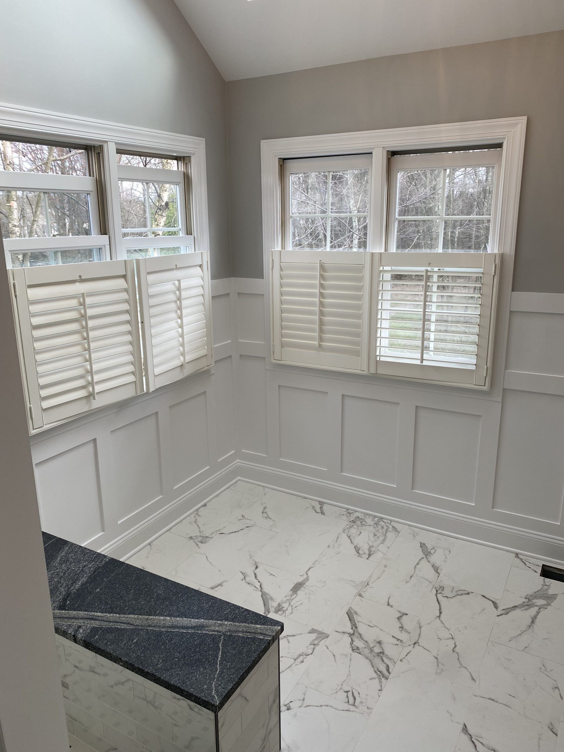 An empty room with a marble floor and shutters on the windows.