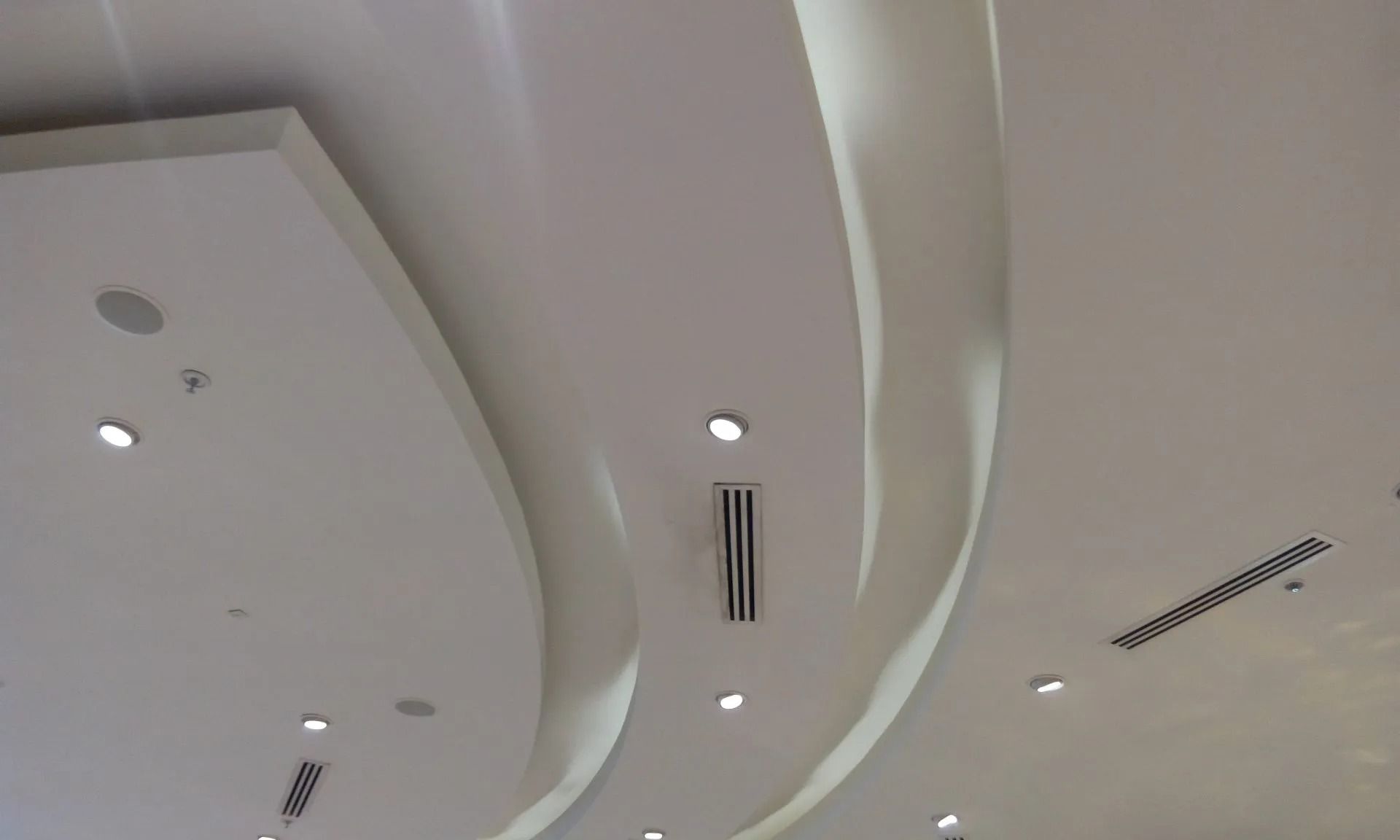 Ceiling with curved white panels, recessed lights, and air vents in a modern interior.