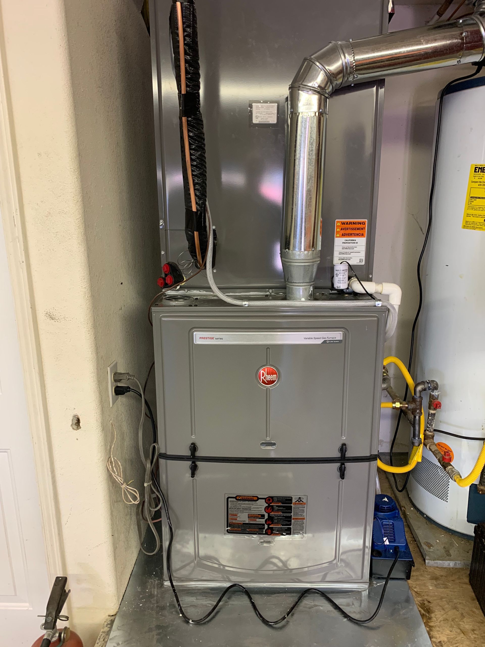Gray HVAC system in a garage next to a water heater, with gas lines and ductwork.
