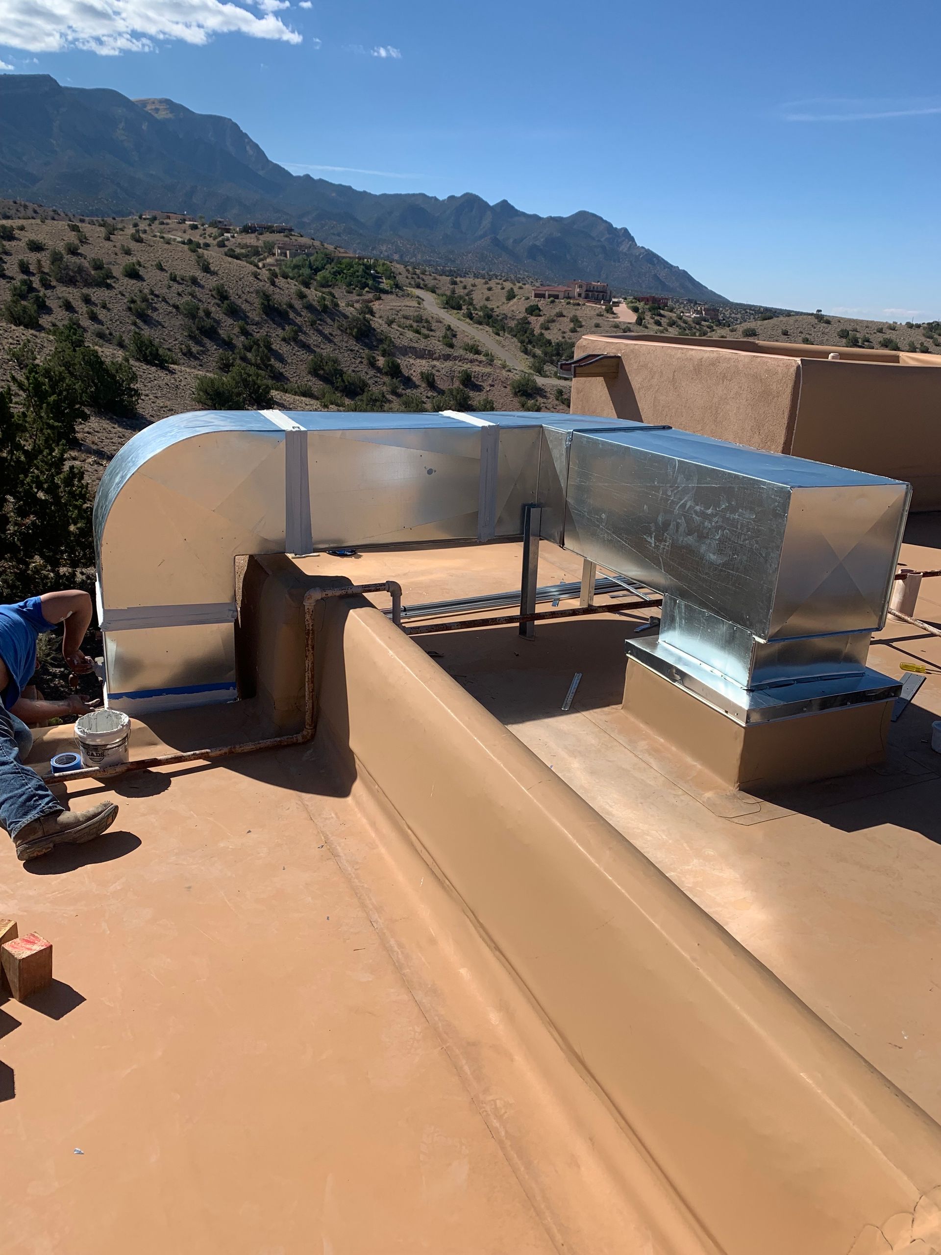 HVAC ductwork on a flat adobe roof with mountains in the background. Sunny, outdoor shot.