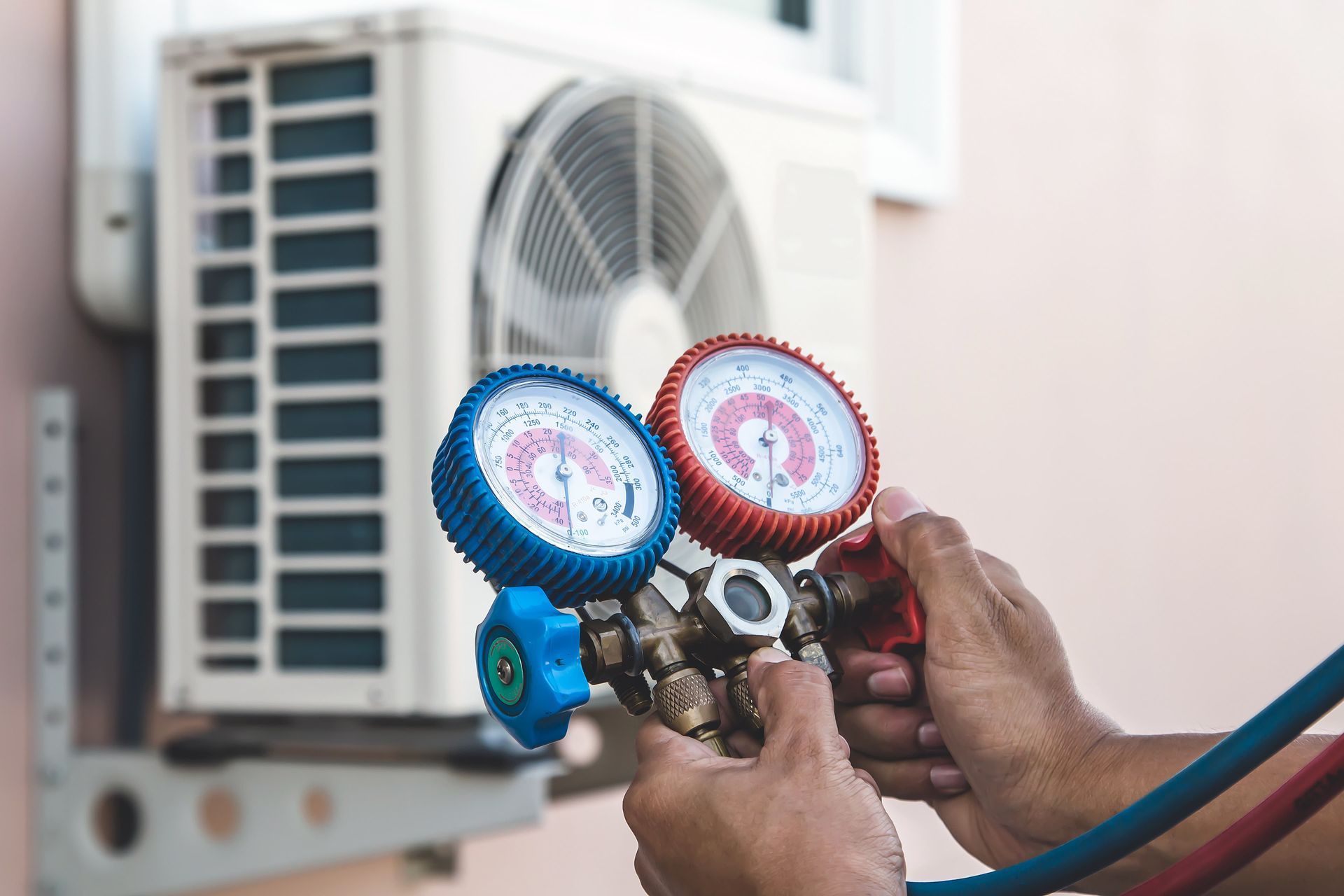 Hands using gauges to service an outdoor air conditioner unit.
