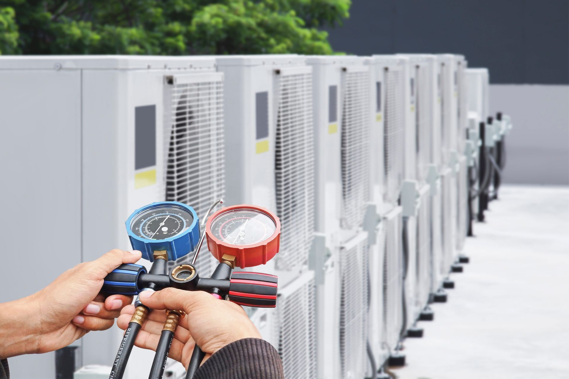 Person using gauges to check a row of HVAC units outside.