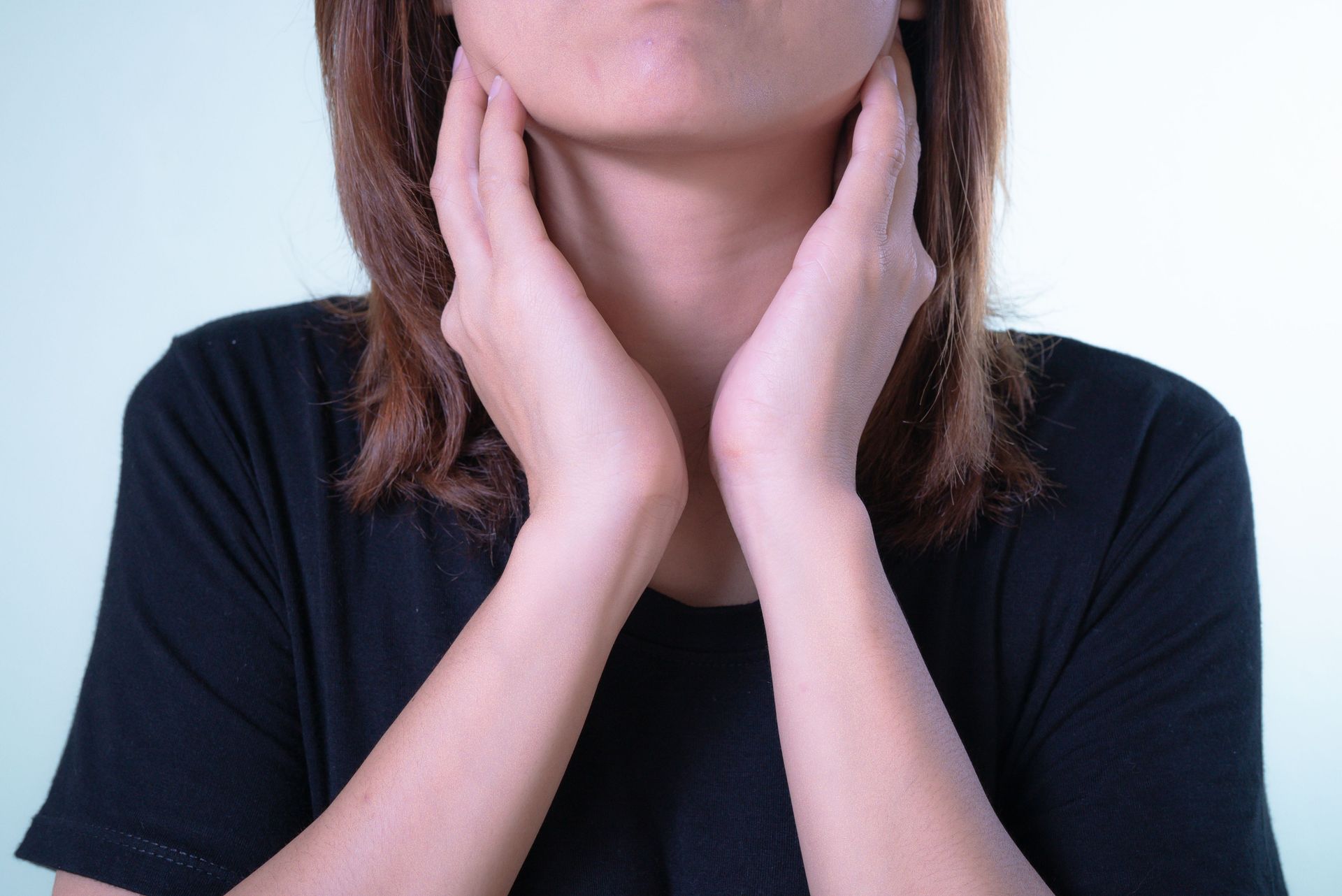 Person holding both sides of their neck, suggesting throat discomfort, against a light background.