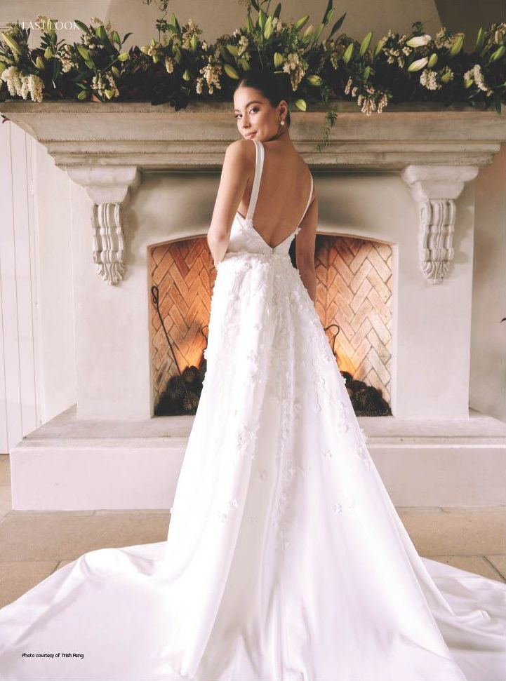 A bride in a long white dress in front of a stone white fireplace