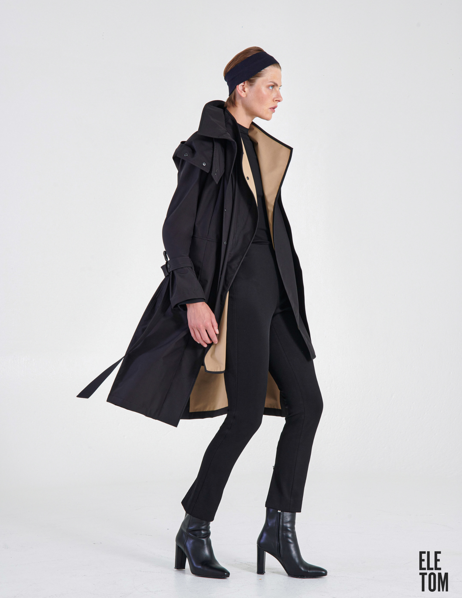 A woman in a black trench coat with a tan lining on the inside lapel and hem. 