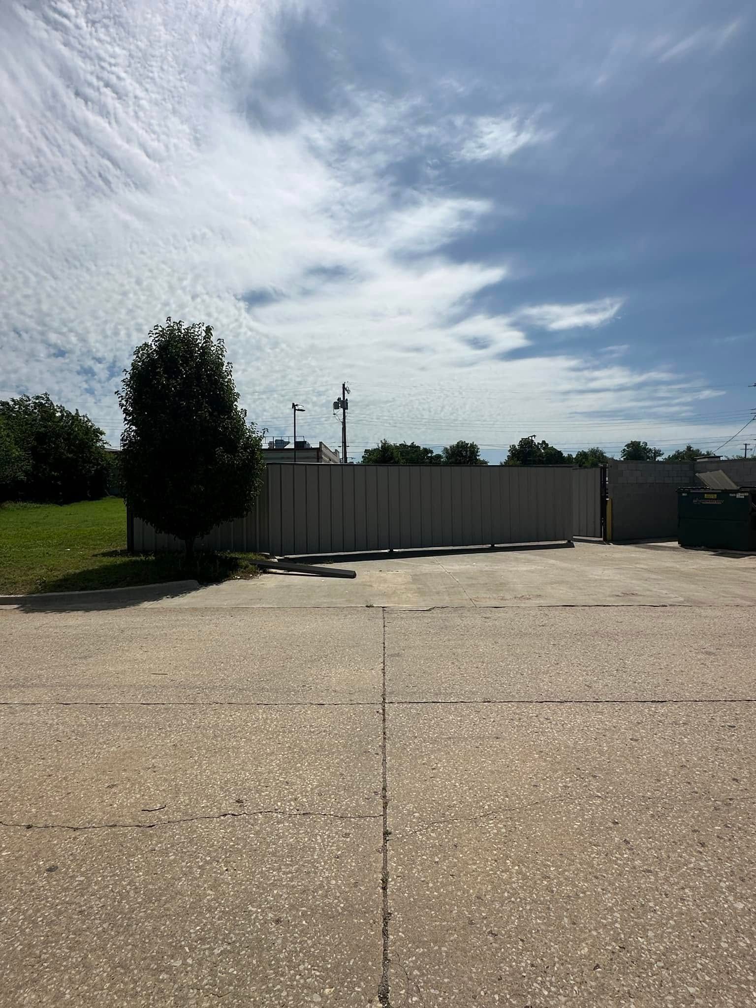 A concrete driveway with a fence and a tree in the background.