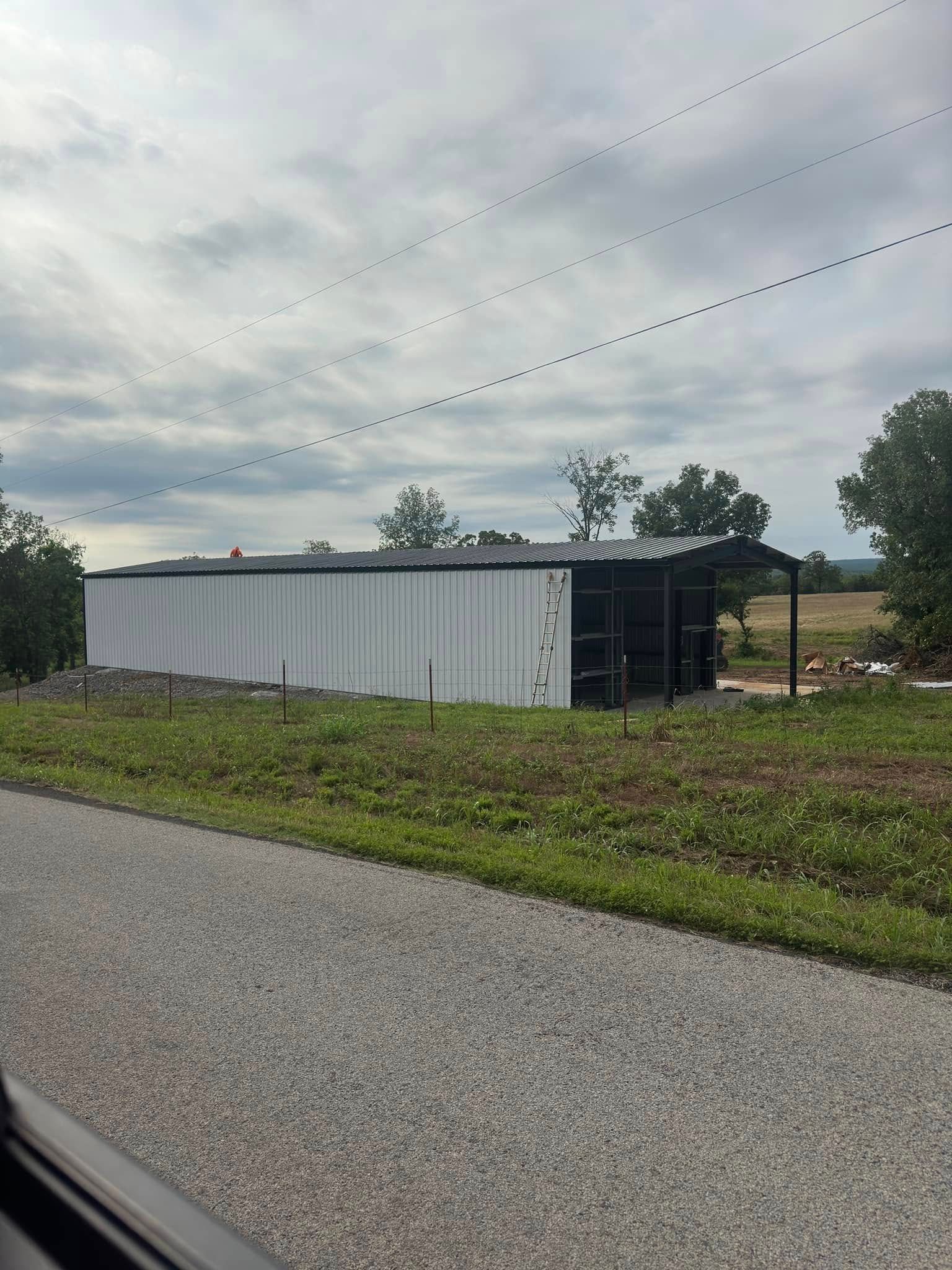 A large white building is sitting in the middle of a grassy field next to a gravel road.