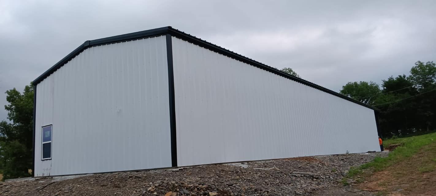 A white building with a black roof is sitting on top of a dirt hill.