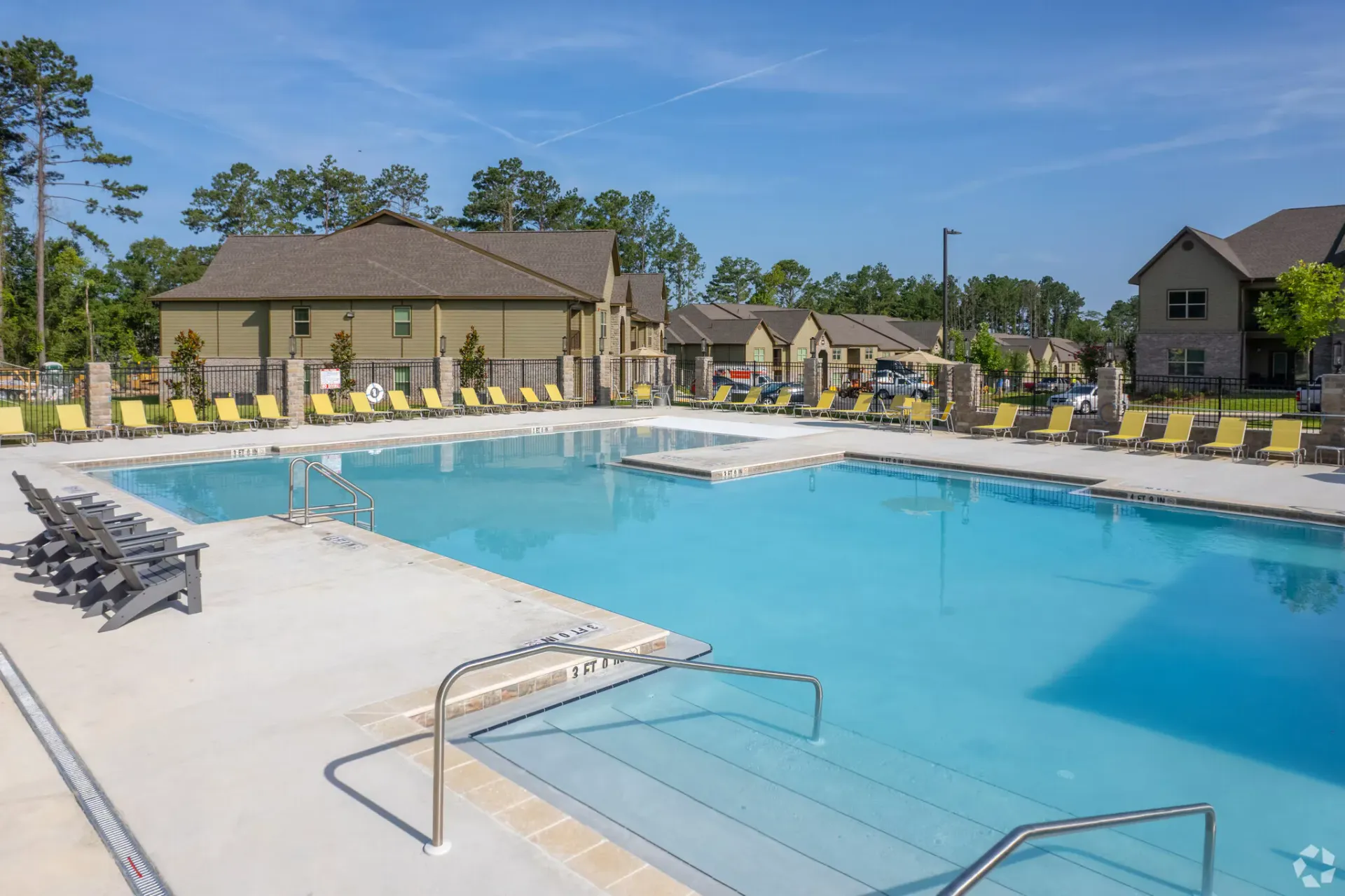 Swimming pool with lounge chairs at a multi-building apartment complex on a sunny day.