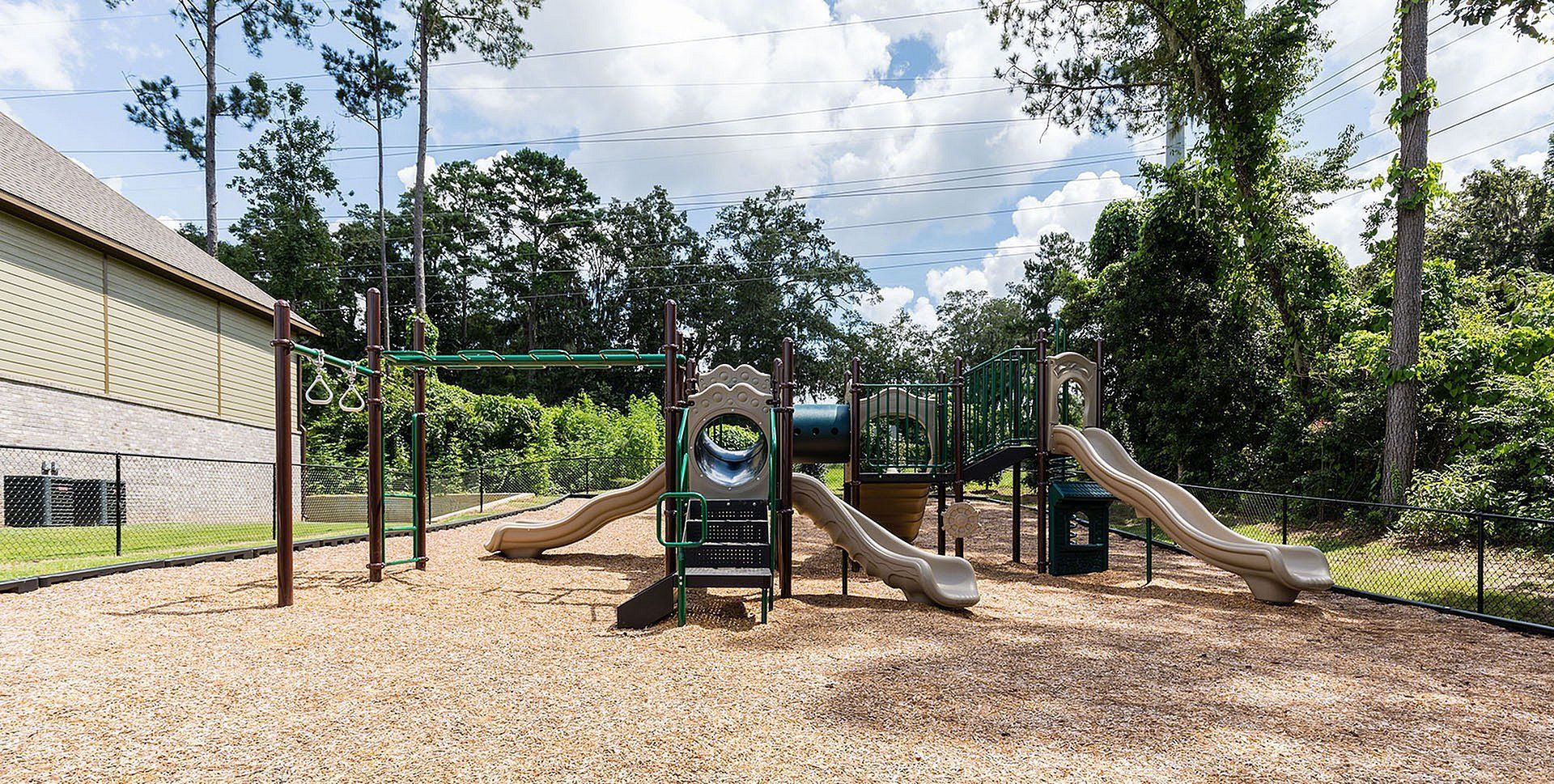 Outdoor community playground with slides and climbing structures inside a fenced area.