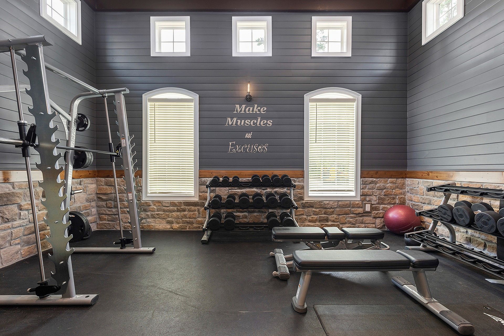 Indoor fitness room with a squat rack, benches, and dumbbells against paneled blue walls.
