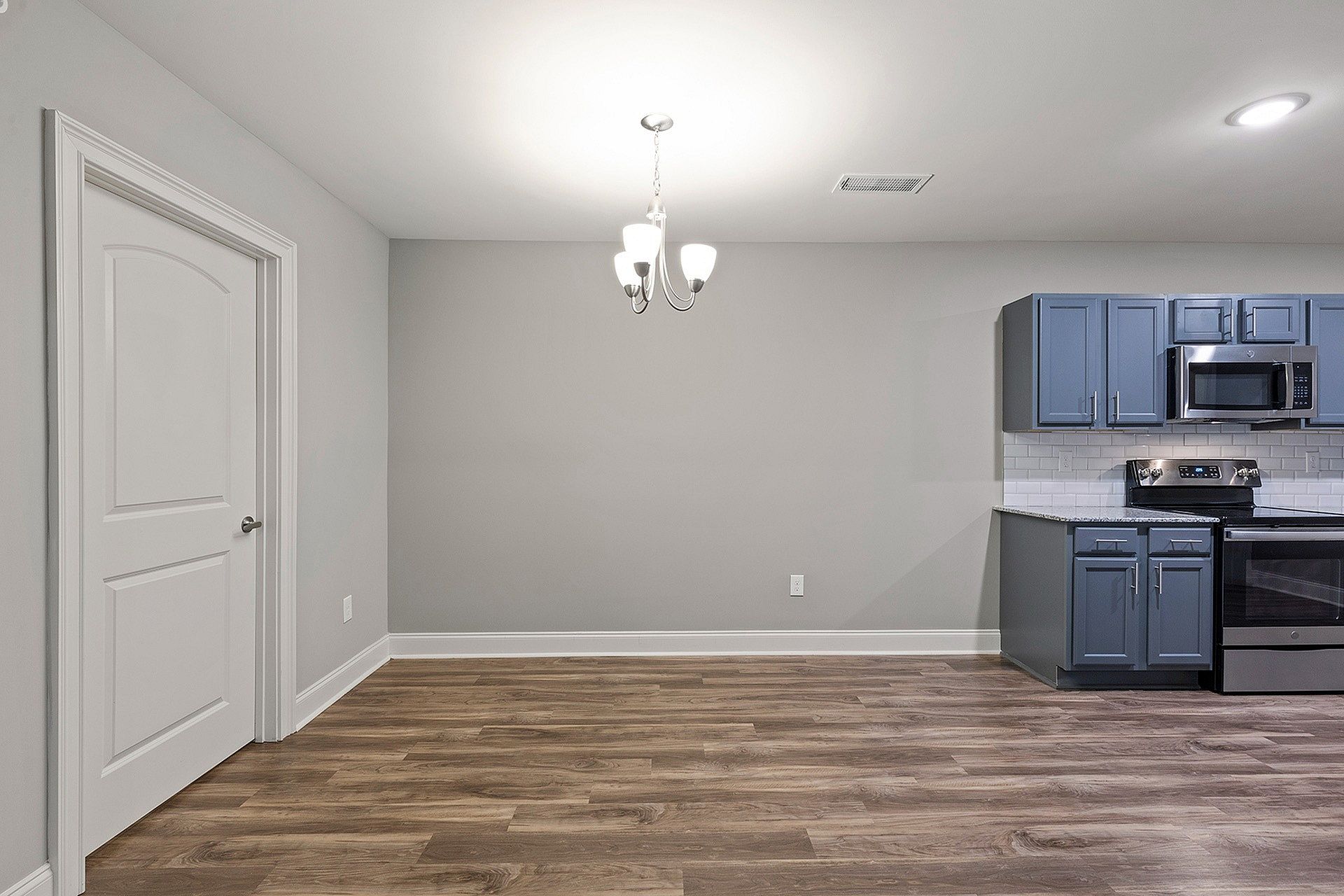 Interior of an apartment kitchen with blue cabinets, stainless steel appliances, and a chandelier.