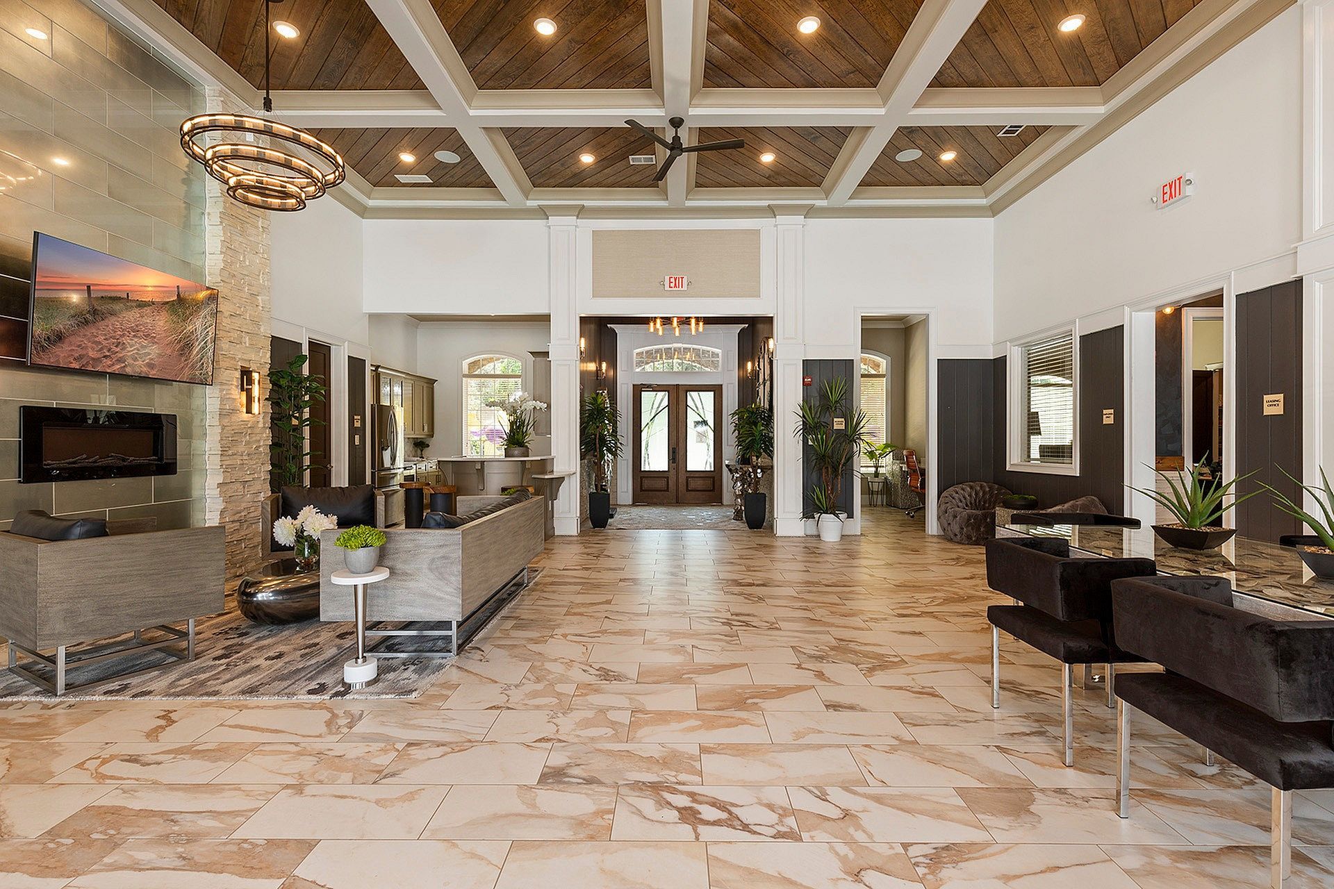 Spacious apartment lobby with seating area, a fireplace, TV, plants, and double doors.