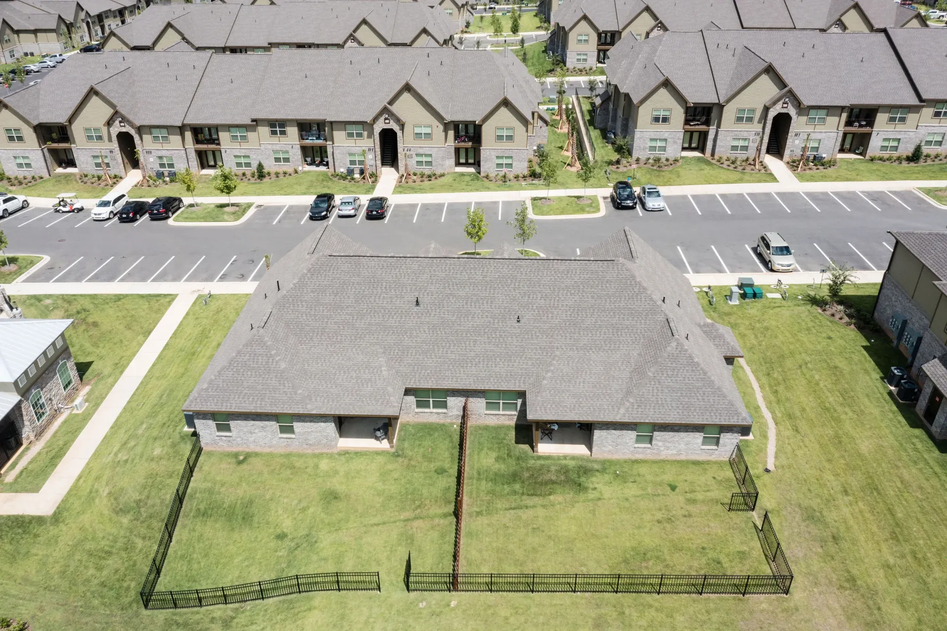 Aerial view of a multi-building apartment complex with parking lots, green lawns, and a central fenced yard.