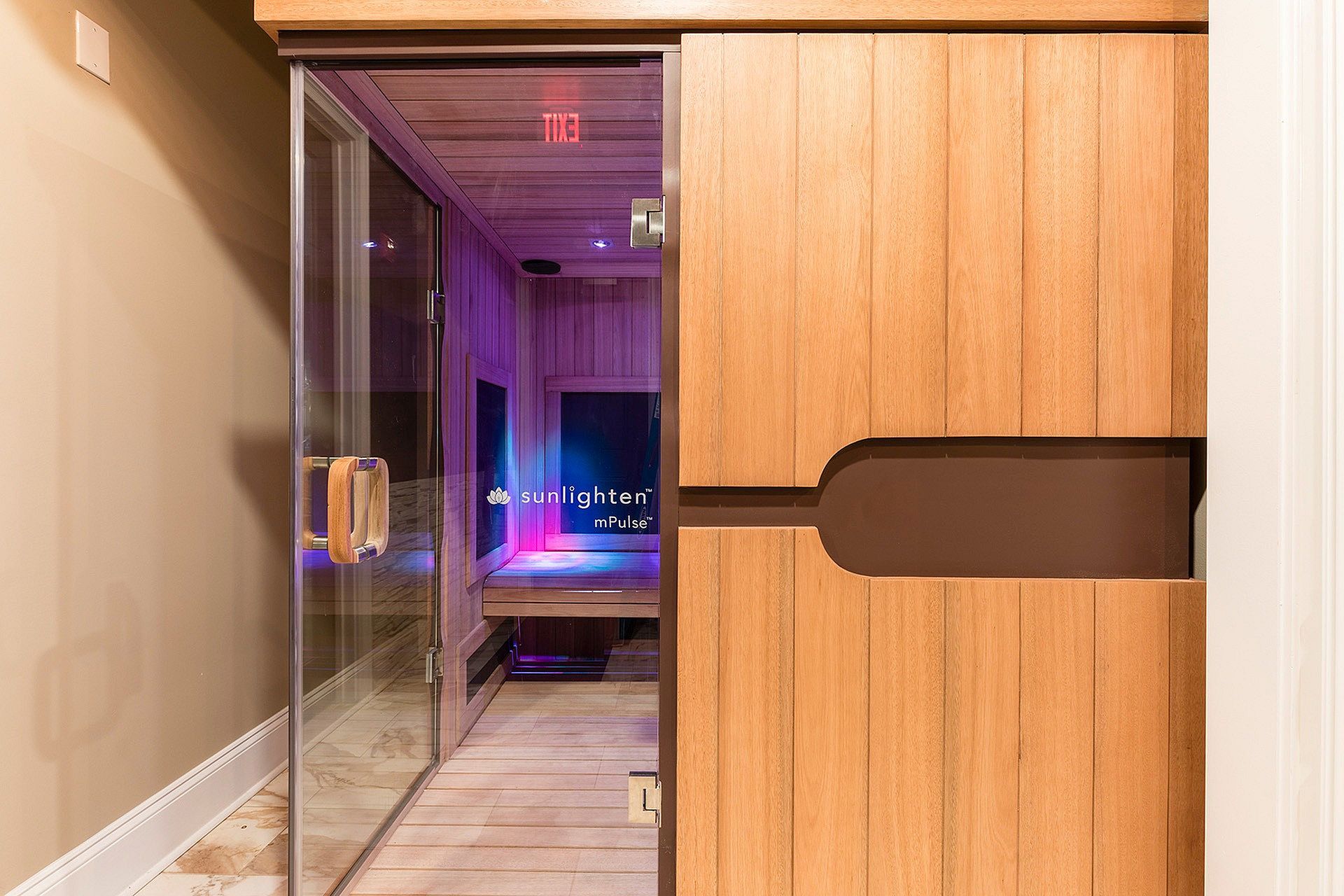 Wood-paneled sauna seen through a glass door with purple lighting.