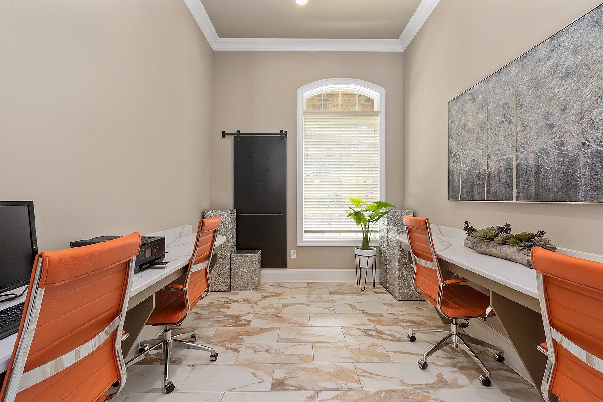 Home office in apartment: two desks, orange chairs, window with blinds, plant, and artwork.