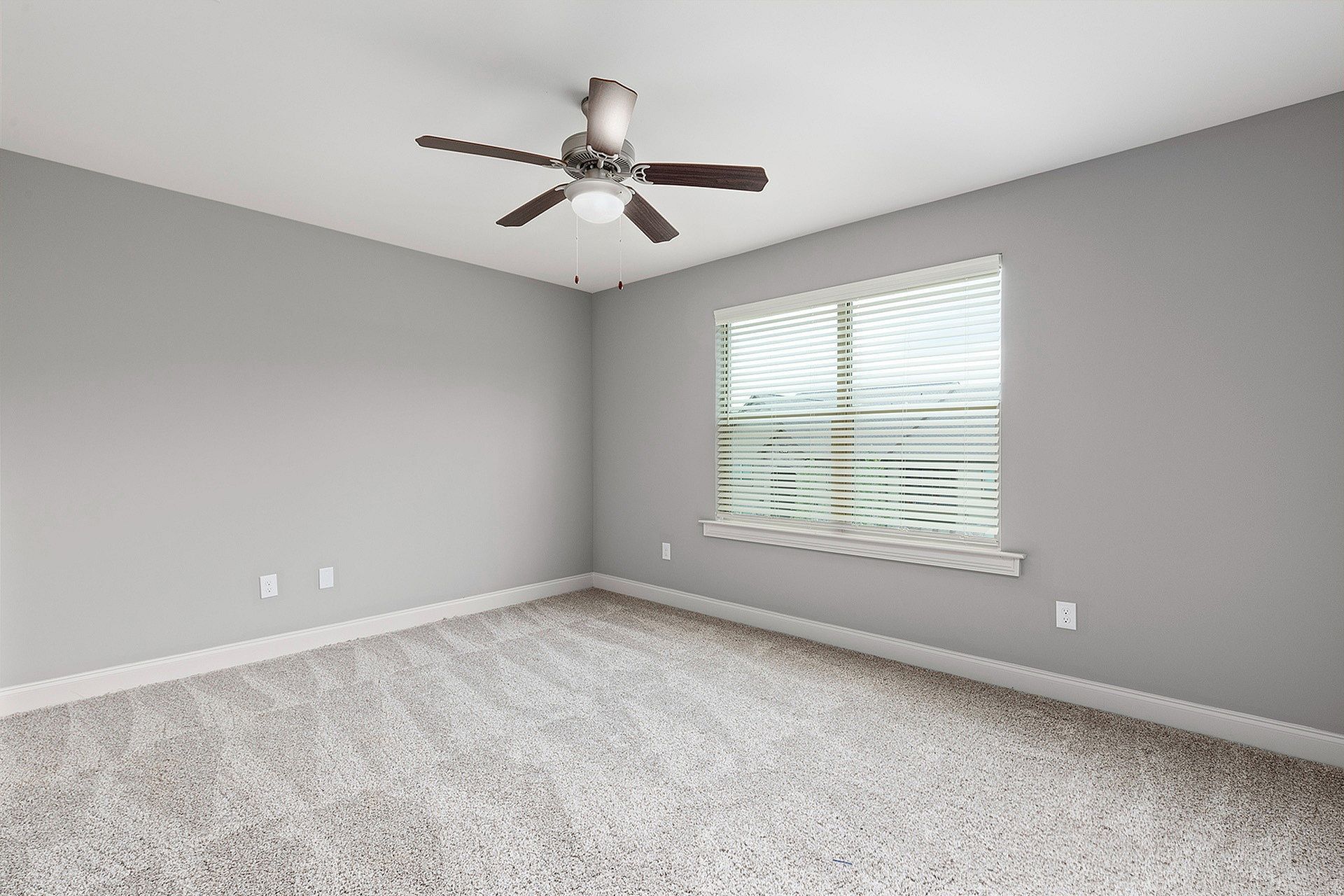 Empty bedroom with gray walls, carpet, a ceiling fan, and a window with blinds.
