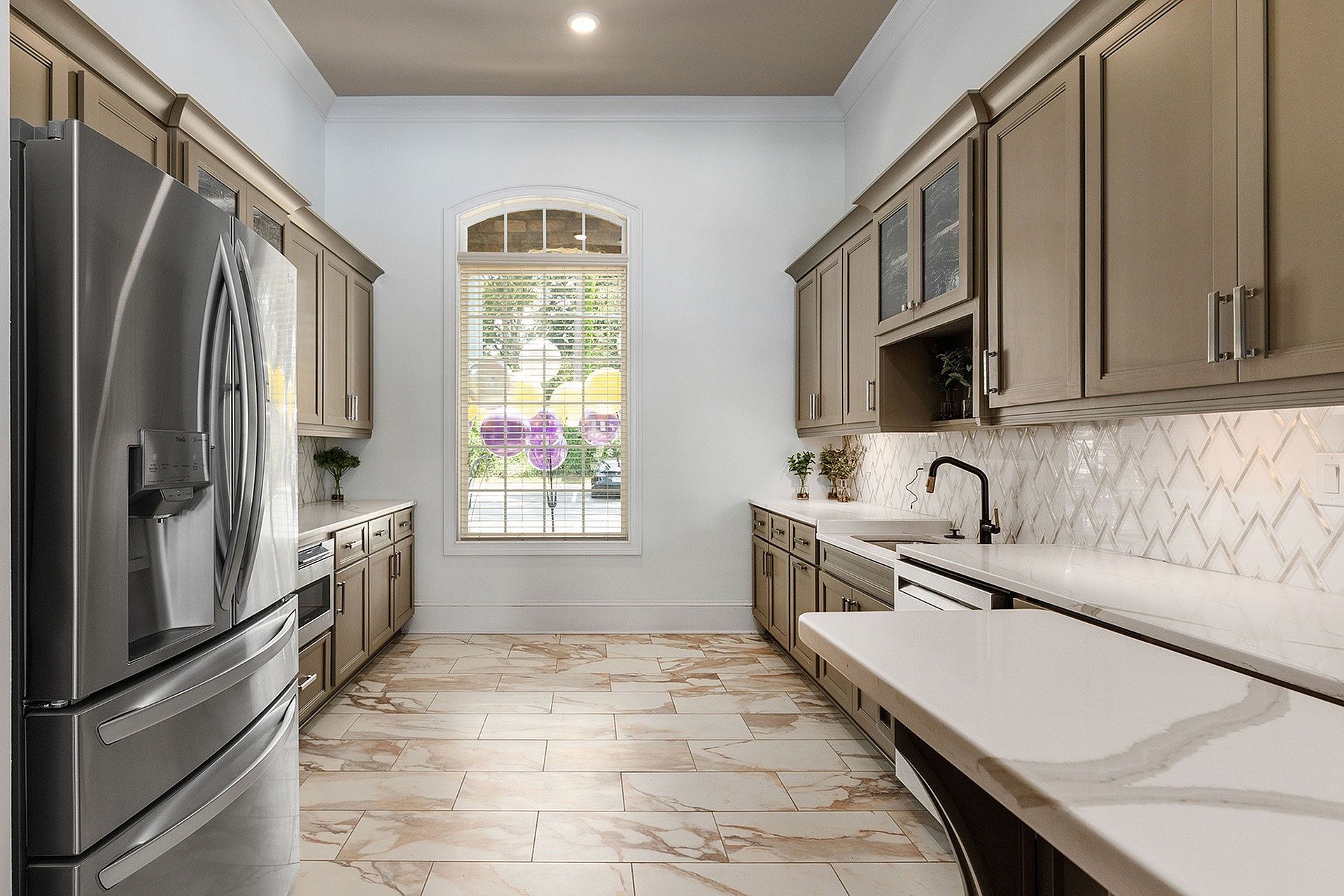 Modern apartment kitchen with stainless steel appliances, beige cabinets, and a window at the far end.