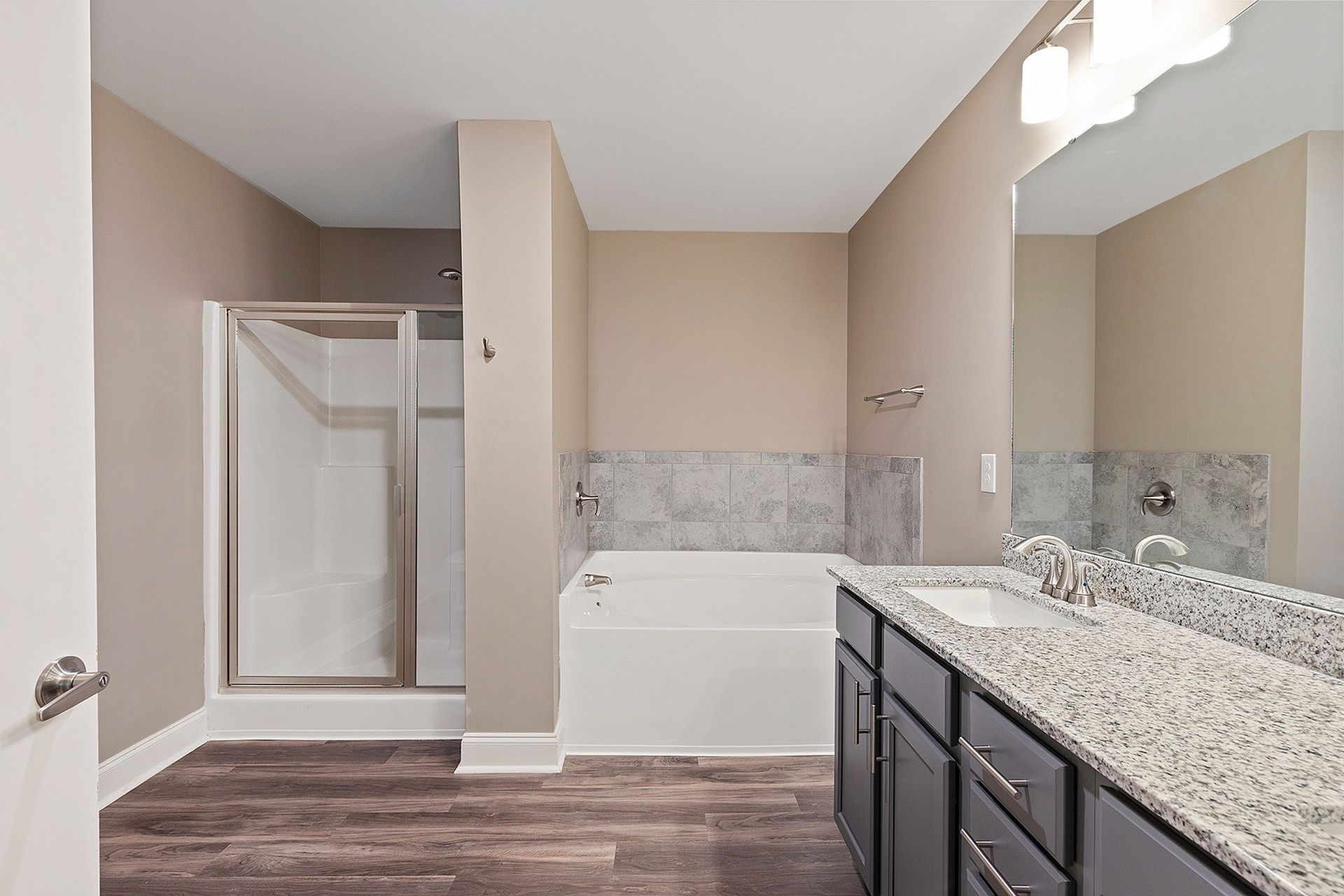 Bathroom in an apartment with a tub/shower, tile surround, granite countertop, and gray cabinetry.