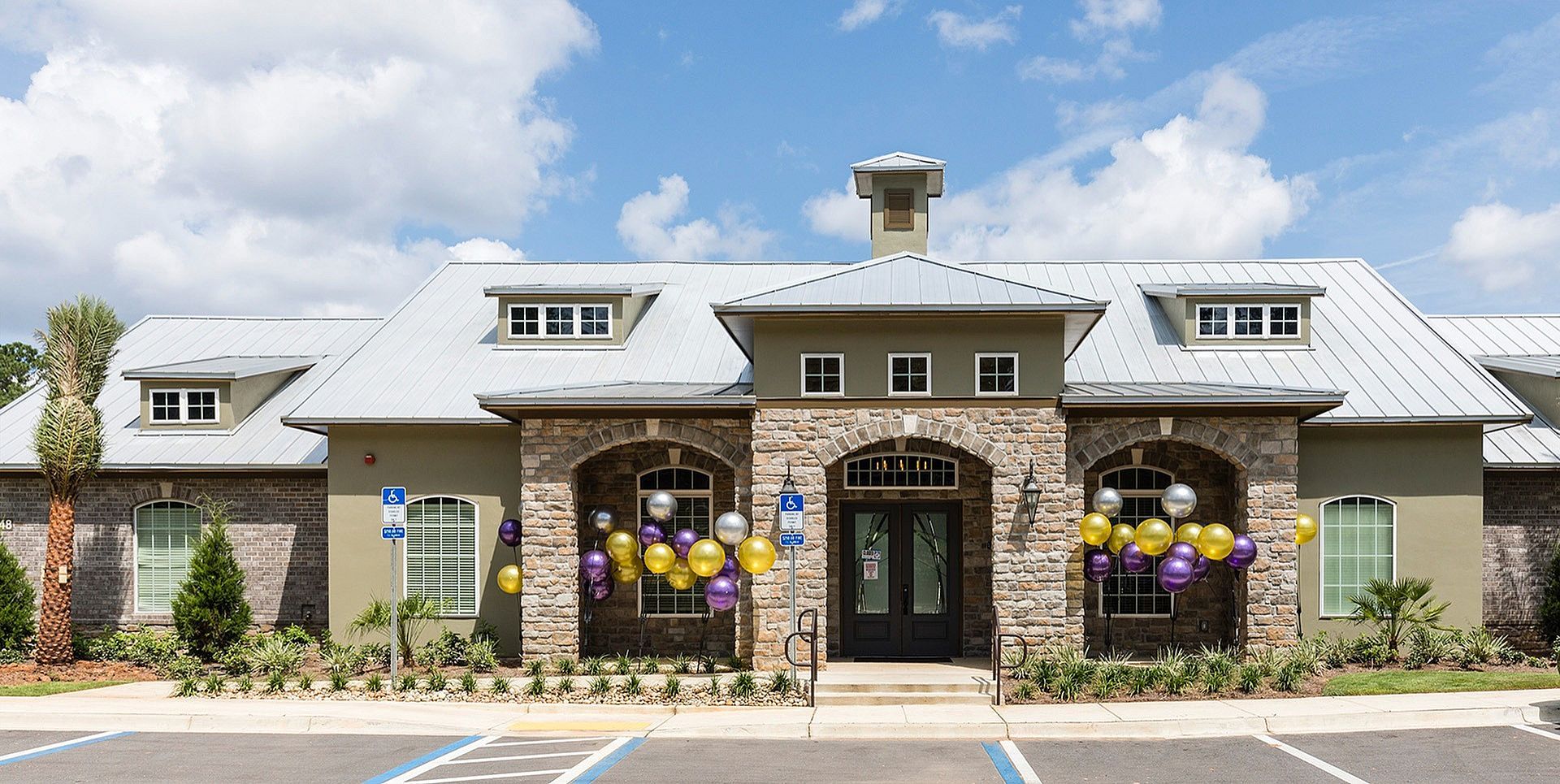 Front exterior of multifamily community building with stone arches and balloons near the entrance.