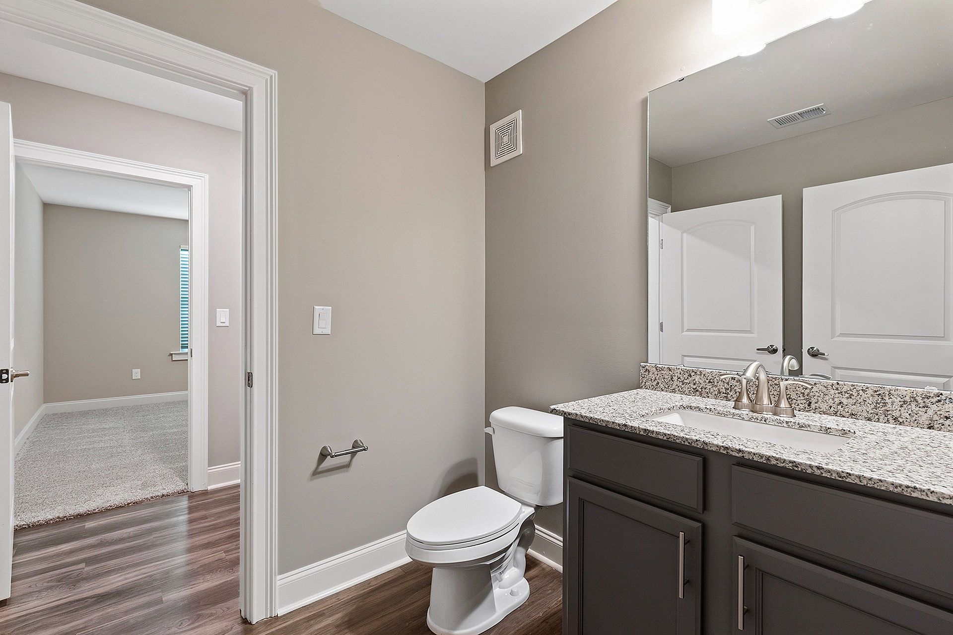 Bathroom in an apartment with granite countertop vanity, sink, toilet, and large mirror.
