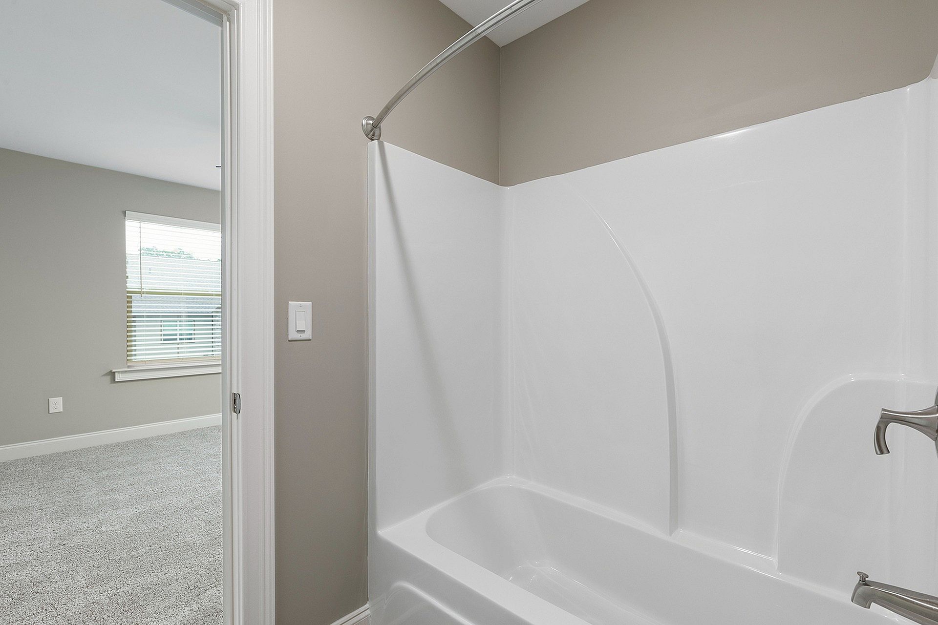 Bathroom with white tub/shower, curved rod, and beige walls.