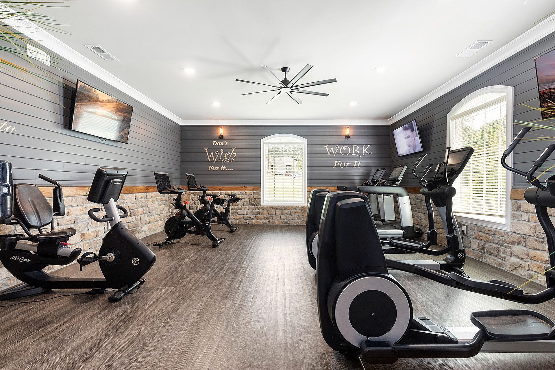 Indoor community gym with cardio machines and wall-mounted TVs.