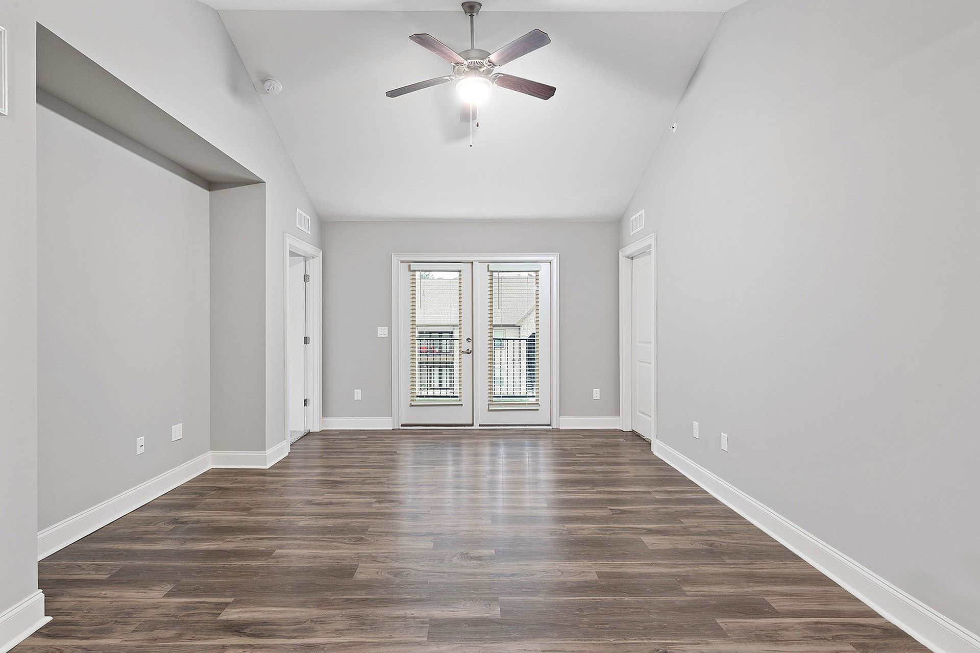 Empty living room with light gray walls, wood-look flooring, a ceiling fan, and French doors leading outside.