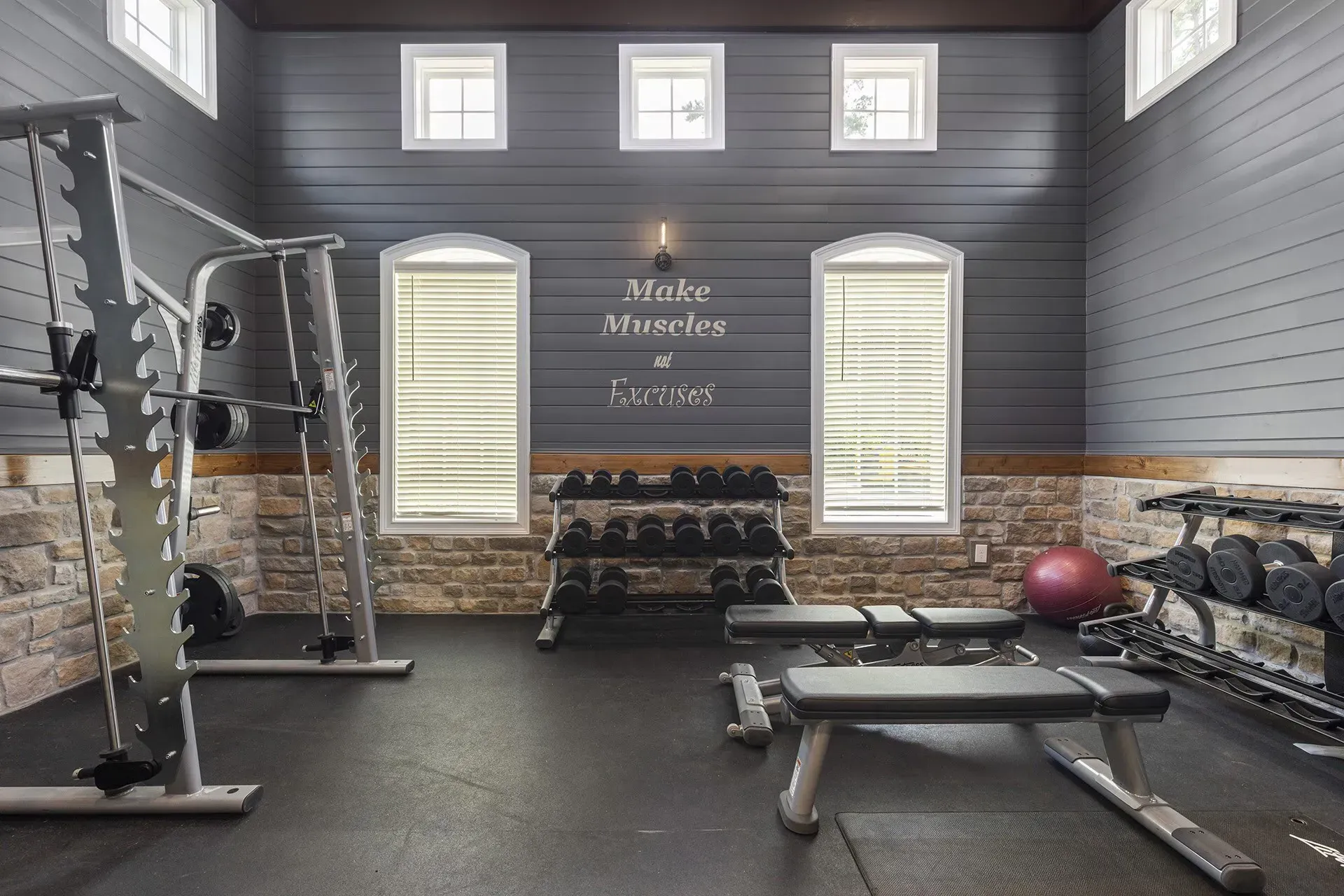 Gym with weight machines, free weights, and bench; windows and a motivational quote on the wall.