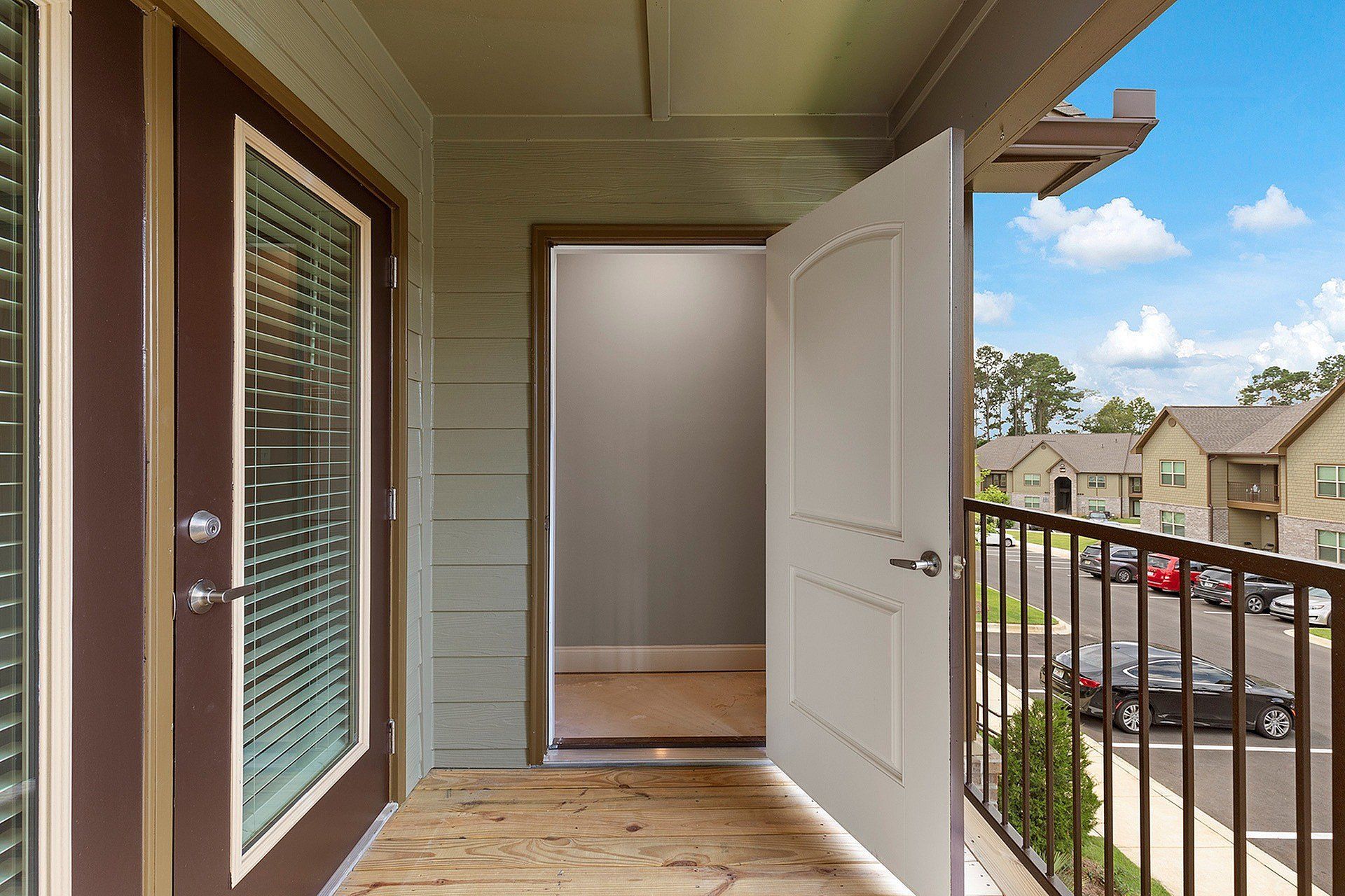 Open balcony door overlooking parking lot and neighboring apartment buildings.