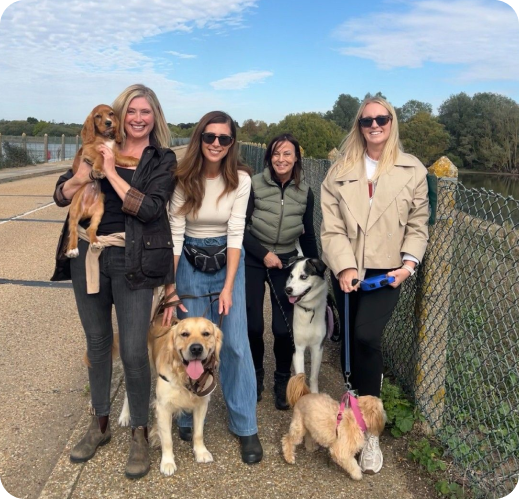 Five people with three dogs posing outdoors by a river on a sunny day