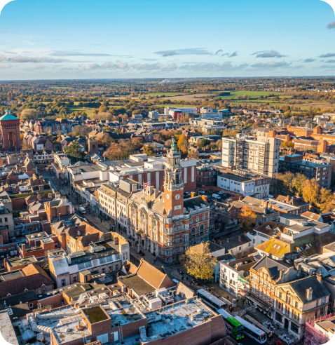 Aerial view of a historic city center with brick buildings, a clock tower, and autumn trees under a blue sky