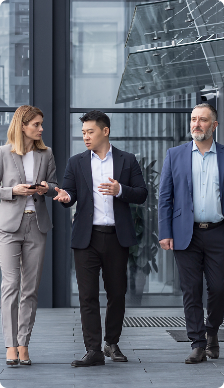 Three businesspeople walking and talking outside a glass office building