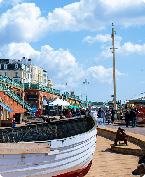 Colorful seaside promenade with a large boat, people walking, and buildings under a blue sky