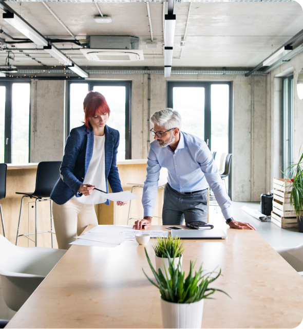 Two coworkers discussing papers in a bright modern office, leaning over a conference table.