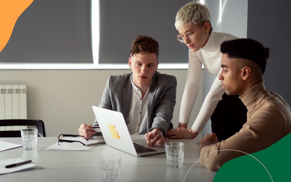Three people in a meeting discussing a laptop at a conference table