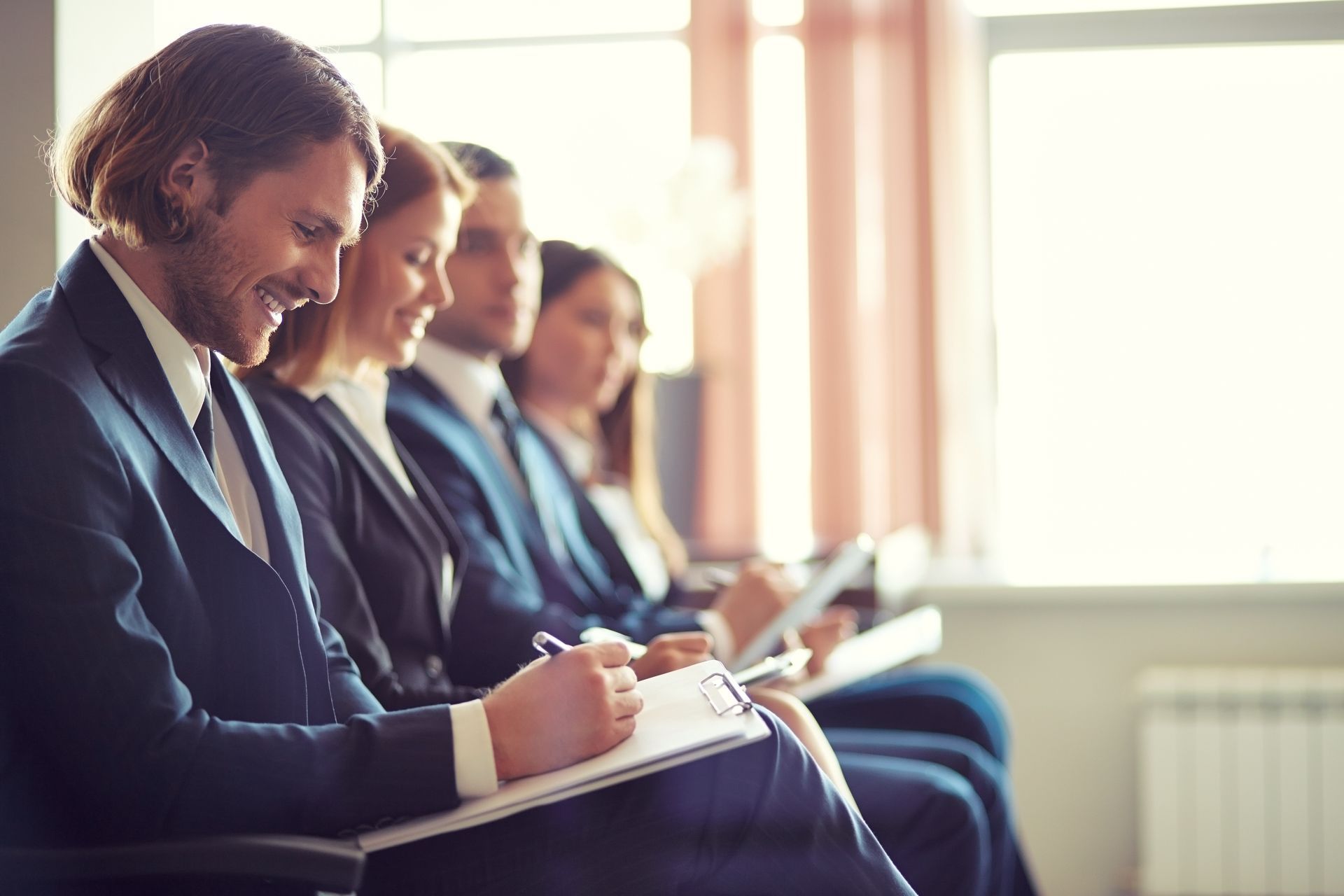 People seated in a row taking notes during a seminar or meeting in a bright room