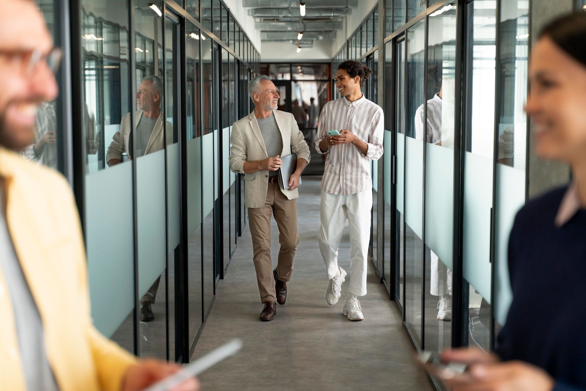 People walking and talking in a glass-walled office hallway.