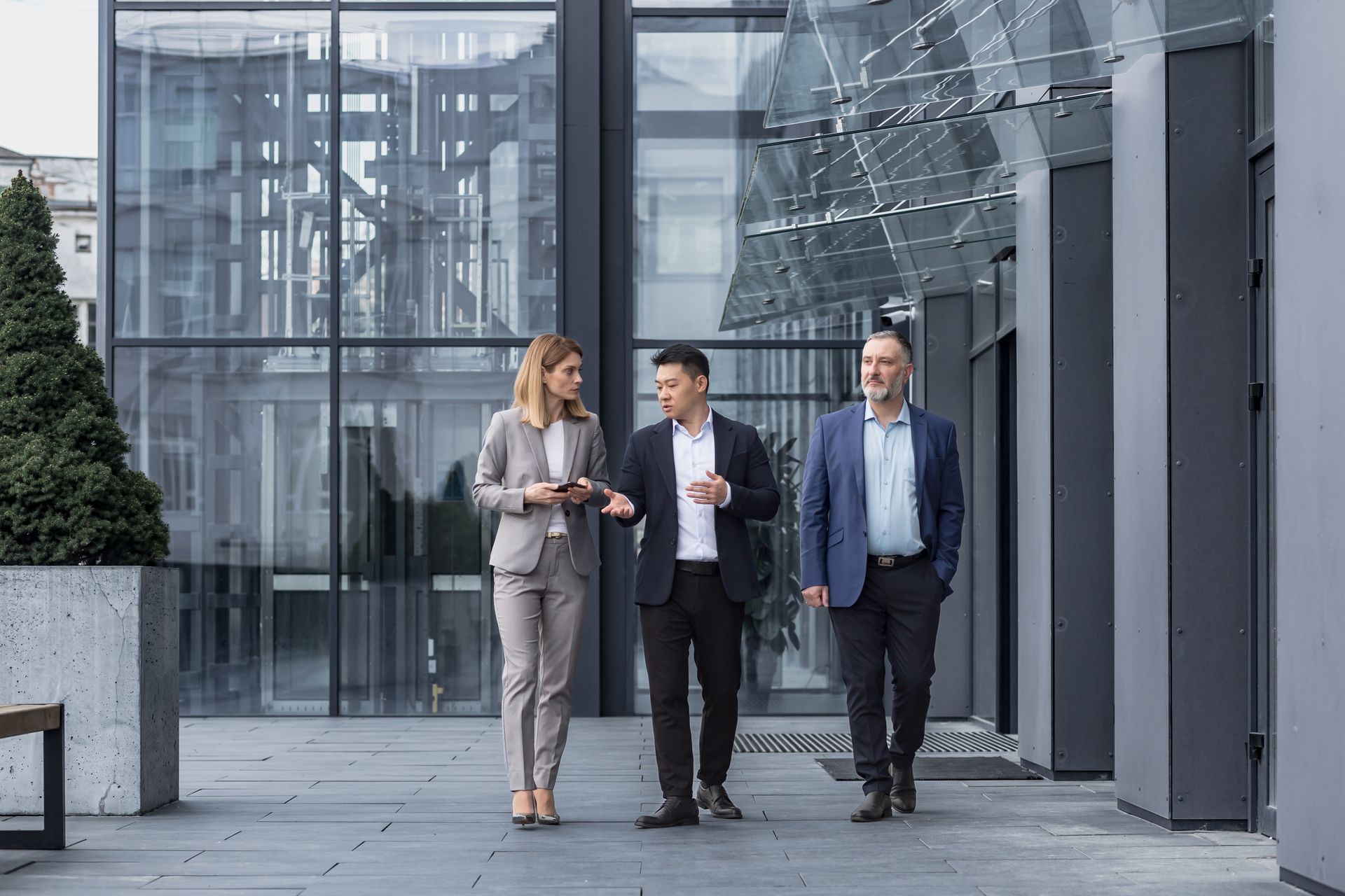 Three businesspeople walking and talking outside a glass office building