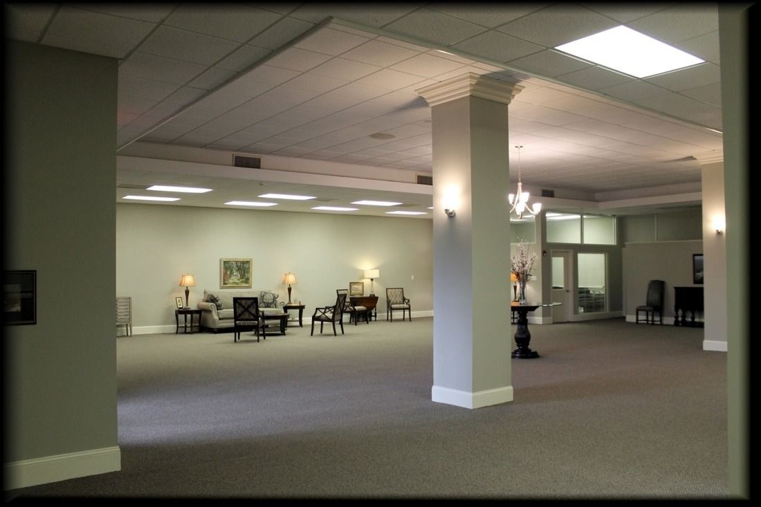 Spacious interior room with seating areas, columns, and a doorway. Neutral colors and overhead lighting.