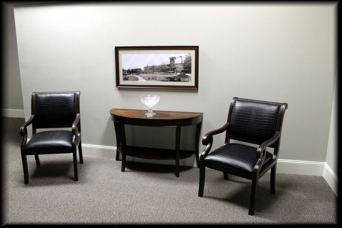 Two black chairs and a half-moon table with a framed picture on a gray wall.