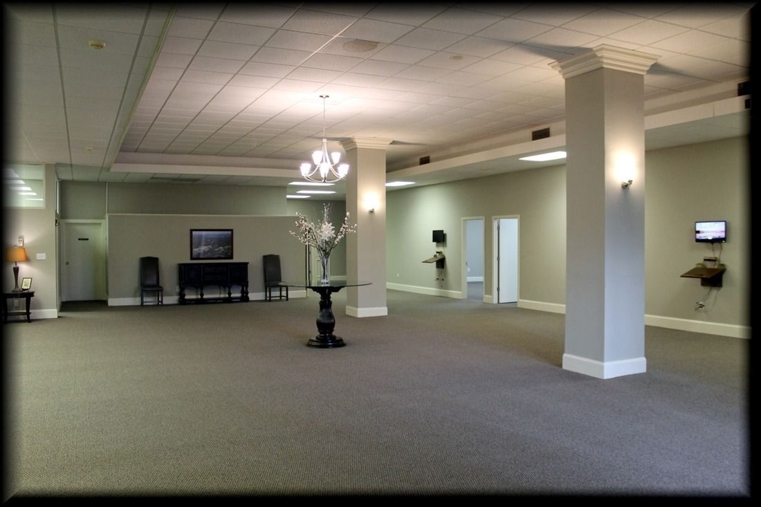 Empty, carpeted room with pillars and chandelier, likely a reception area.