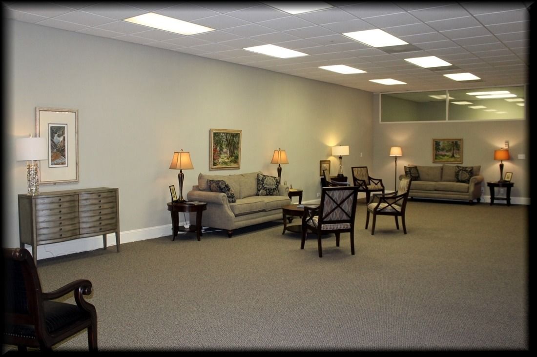 Empty waiting room with couches, chairs, lamps, art, and beige carpet.