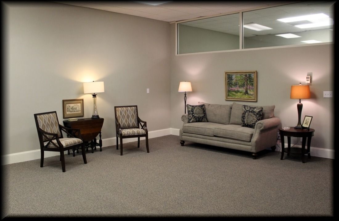 Gray-walled waiting room with seating: sofa, chairs, lamps, and a small table.