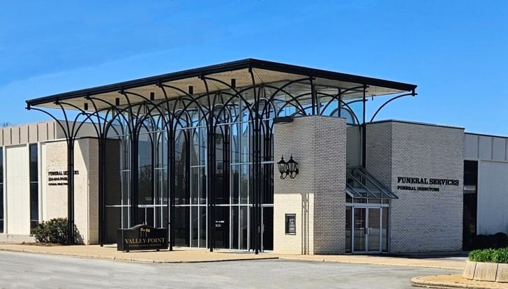 Funeral home with a modern architectural style; light-colored brick exterior, glass front, and a unique canopy supported by tall, thin columns.