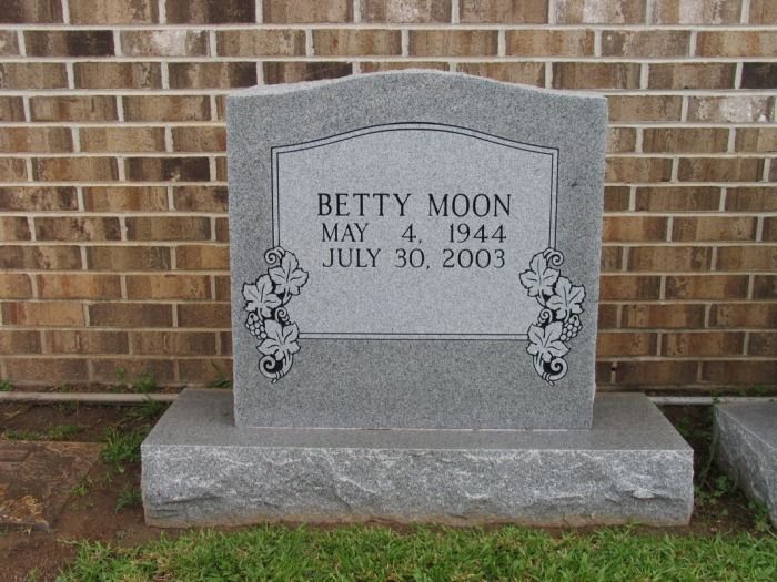 Gray granite headstone for Betty Moon, born May 4, 1944, died July 30, 2003, against a brick wall.