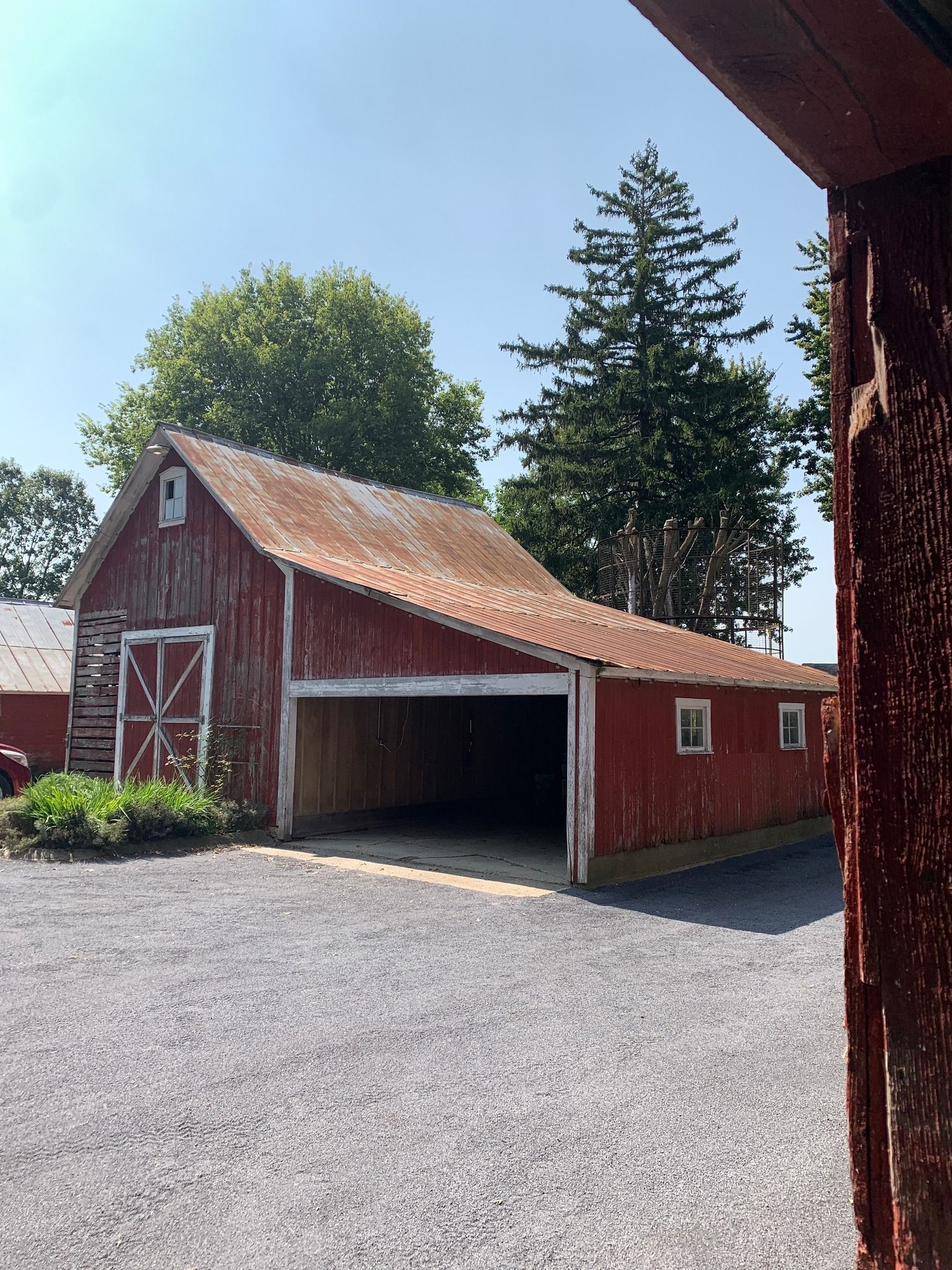 Red barn with white doors and weathered roof under a bright blue sky.